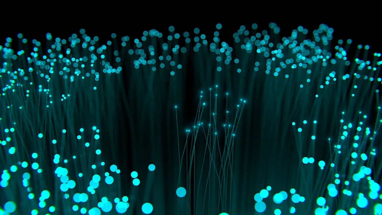 Illuminated fiber optic cables carrying light signals through a network junction in a modern datacenter facility